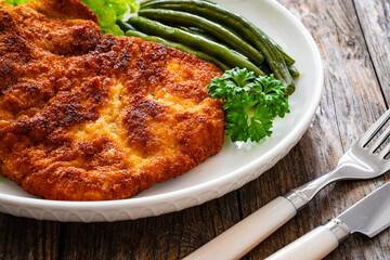 Breaded fried pork chop with cooked green beans on wooden table

