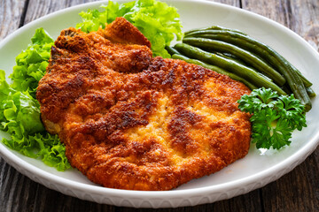 Breaded fried pork chop with cooked green beans on wooden table
