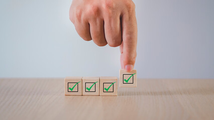Businessman hand selecting wooden block checklist and green hand icons on table background....