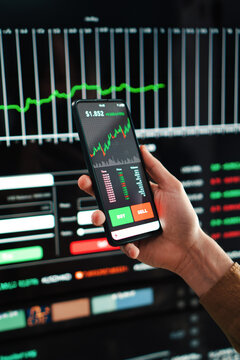 Vertical portrait of crypto trader broker using a cell phone financial app to buy or sell shares of stock market. Investment concept. Hand holding a smartphone with banking blockchain application