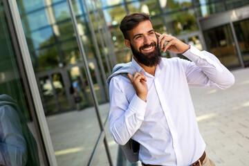 Handsome successful businessman using smartphone in front of office. Technology business concept.