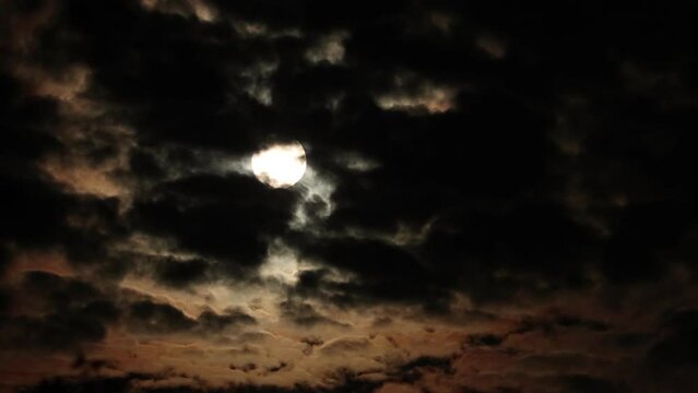 Full Moon on dark cloudy night sky. Clouds passing by the Moon in spooky feeling like thriller and horror films. Real shot with natural black clouds