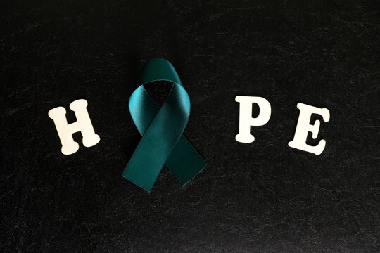 Teal ribbon color isolated on dark black background. Ovarian cancer awareness and hope concept.	