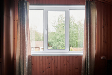 Closed plastic window and wall inside the room. Window with view of summer sunny backyard of wooden...