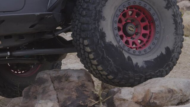 Slow motion of wheel on jeep four wheeling over rocks in desert terrain