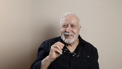 smiling elderly man holding glasses and smiling, low angle portrait, light background, studio