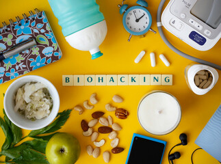 Biohacking flat lay with letters "Biohacking" on yellow background. Health improvement concept aiming at healthy food, exercise, supplements, probiotics, meditation, hydration and self measurement.