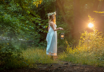 girl is standing in the forest  an old kerosene lamp in her hands, with a wreath of daisies on her head. - obrazy, fototapety, plakaty