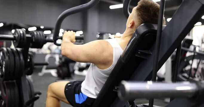 Man exercising, doing chest press with weight discs in gym. Exercise machine with heavy weight lifts