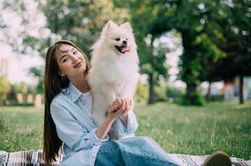 Young woman with her cute dog in park. Pomeranian Spitz with his owner are sitting on the grass.