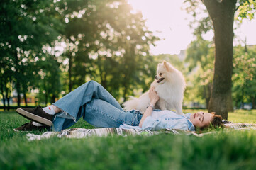 A young woman lies on the grass and holds her Pomeranian dog in her arms.