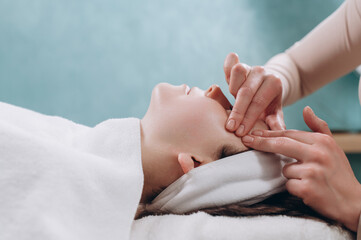 The beautician makes a deep facial massage to a young woman. Face massage technique against aging. Close-up.