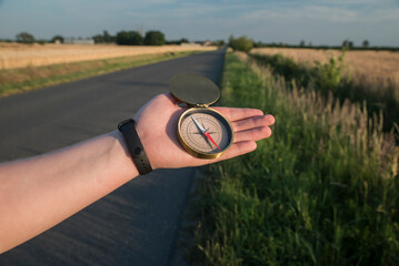 Kompas leżący na wyciągniętej ręce na tle prostej szosy oraz pól porośniętych zbożem.