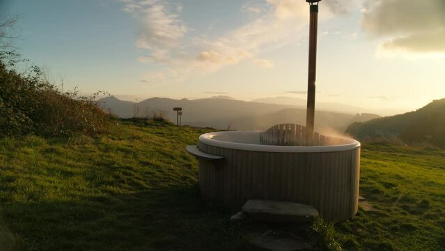 Majestic shot of picturesque hot tub or Dutch tub surrounded by nature and mountains at sunset. Perfect destination for an epic outdoor getaway or relaxing holiday. Glamping or spa natural hotel.