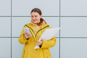 Young woman in yellow uniform using smartphone and holding package. Delivery service holding to sent a white package letter, for mockup