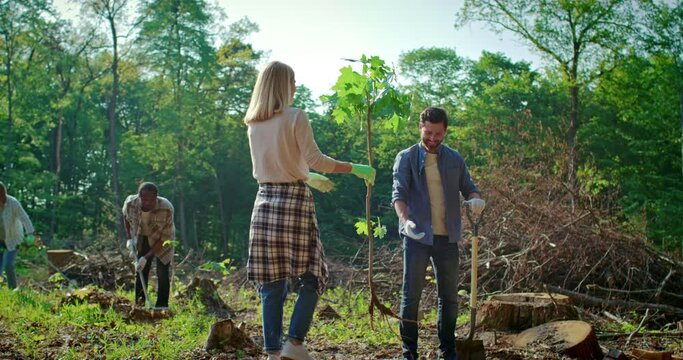 Young people girls and boys volunteers outdoors helping nature planting trees together pouring water from watering can on ground smiling joyful cooperation. Environmental protection.