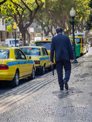 Man wearing suit walking by a row of yellow taxis, Funchal, Madeira