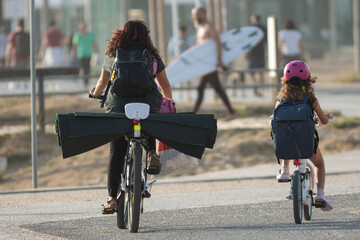 Tourists ride a bike with yoga mats and go to the beach holding a surfboard