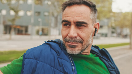 Mature man wearing casual clothes in wireless earphone enjoying music while sitting on park bench, bottom view, soft focus