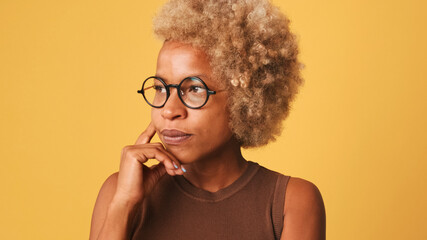 Close-up profile of girl in glasses, wearing brown top looks somewhere pensively thinks about something tries to make decision in mind, isolated on orange background