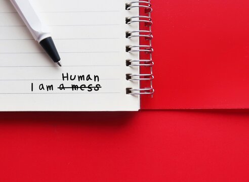 Notebook on red copy space background with handwriting I AM A MESS, changed to I AM HUMAN - to overcome negative self talk or inner voice critic, change to positive thought to boost self esteem