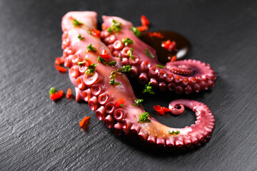 Octopus serving with vegetables, sea food. Freshly boiled octopus tentacles dish on a dark stone slate plate, Asian, Mediterranean cuisine, dinner. Restaurant menu, on black background