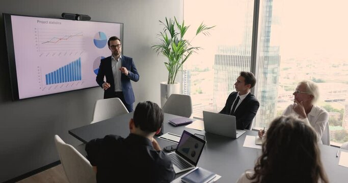 Serious young businessman selling successful company. Speaker presenting project marketing report to partners, investors on meeting for negotiations, speaking at electronic board