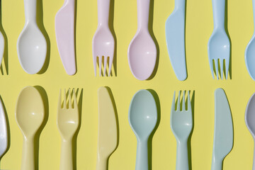 close up pattern of multi use plastic cutlery on a pastel yellow background