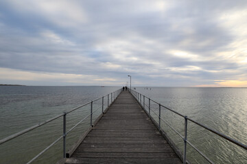 Fototapeta na wymiar View of jetty leading out to ocean beneath cloudy sky at sunset