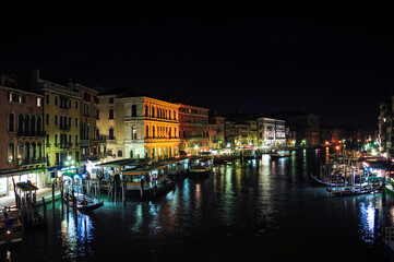 Night view of the Grand Canal in Venice, with many gondolas and boats docked on the banks of the river