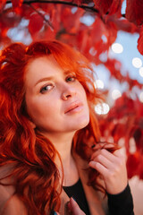 Portrait of beautiful red-haired woman wearing nose ring in red autumn leaves