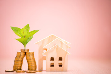 Stack gold coin with plant growing value on the top and the stack wooden house on the pink background in the office, Business investment or loan for real estate concept.