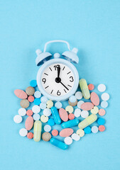 The Medicine time. High angle view of colorful medicines and pills on alarm clock on the blue background.
