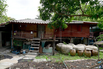 Fototapeta na wymiar BANGKOK, THAILAND - JULY 14, 2023: An old wooden house raised on a high platform with several big earthen jar for water placed in front of the house natural background.