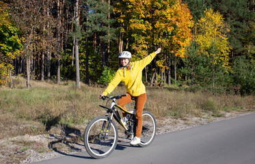 Fototapeta premium young woman on a bicycle rides in an autumn park on a sunny day. Feeling of freedom and joy. Active lifestyle. having fun on an orange autumn background of nature