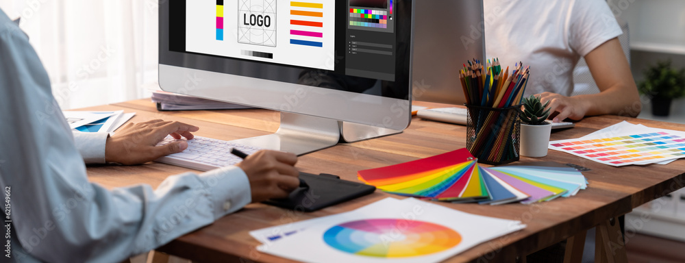 Poster Graphic designer work on computer laptop and with graphic drawing pen while brainstorming unique design with professional graphic team in modern digital studio workplace. Panorama shot. Scrutinize