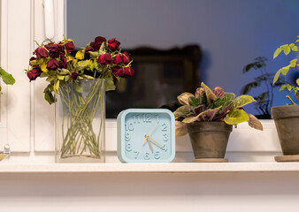 A comfy house room interior, decoration gadgets, clock and flowers in front of the window, group of objects closeup detail, nobody, no people, evening, night, comfy decorative details inside the house