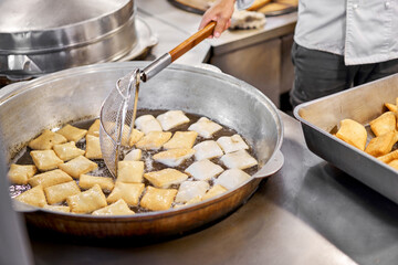 Male cook preparing delicious National Kazakh pastries baursak. street cafe. Fry dough in boiling oil in a frying pan.