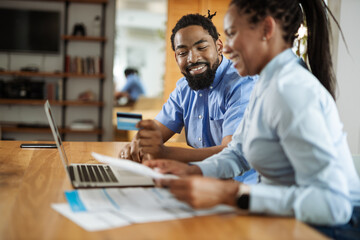 Happy black couple paying their bills with credit card over a computer at home