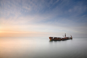 an wrecked boat in a calm sea with soft water and soft clouds  