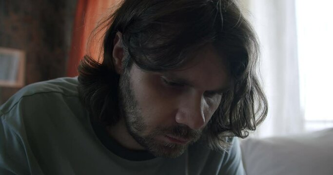 Sad upset pensive man with long hair in dark room. Man in depression, mental health concept
