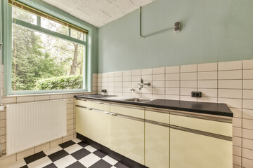 an empty kitchen with black and white tiles on the floor in front of a large window looking out onto trees