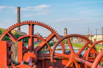 Red industrial gears with nineteenth century brick mill building in background in Lawrence, Massachusetts.