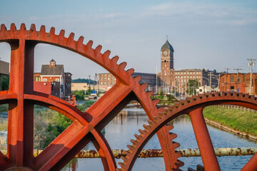 Red industrial gears with nineteenth century brick mill building in background in Lawrence, Massachusetts. - Powered by Adobe