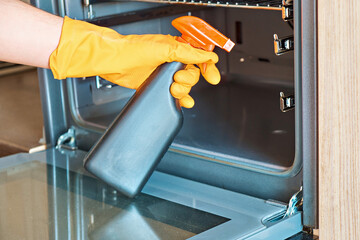 A man wearing protective gloves sprays chemicals to clean the glass in the oven door. Close-up