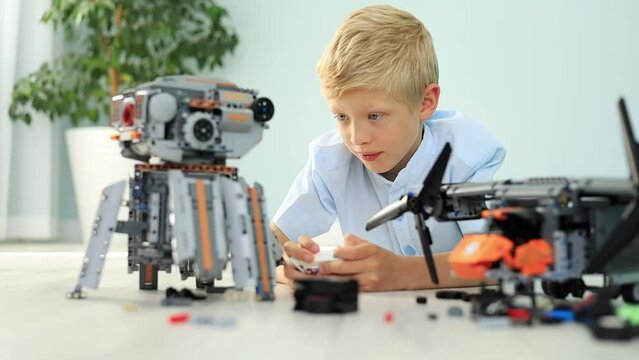 a joyful child boy is playing a robot from a radio-controlled constructor with a remote control, assembling it from the details of the house on the floor, a blonde child is playing at home