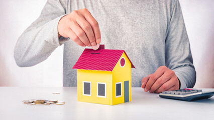 Hand putting coin in house piggy bank. Saving money or home investment. House financial concept.