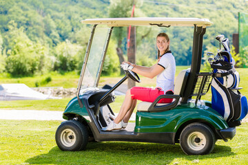 Smiling young woman driving a golf cart along a course while enjoying a round of golf on a sunny day
