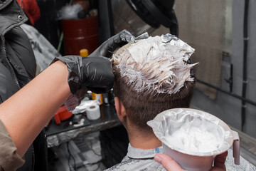 Hands of a professional barber in gloves in the process of coloring hair with dye at work in a hairdresser