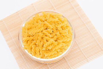 Uncooked Chifferi Rigati Pasta in Glass Jar on Bamboo Mat on White Background. Fat and Unhealthy Food. Classic Dry Macaroni. Italian Culture and Cuisine. Raw Pasta